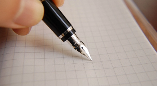 Eine Hand hält einen Füller, der auf einem weißen, kariertem Blatt liegt.