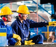 Ein Mann und eine Frau sitzen in blauer Arbeitskleidung und mit gelben Helm vor einer Maschine in einer Halle.&nbsp;&copy;&nbsp;pixabay